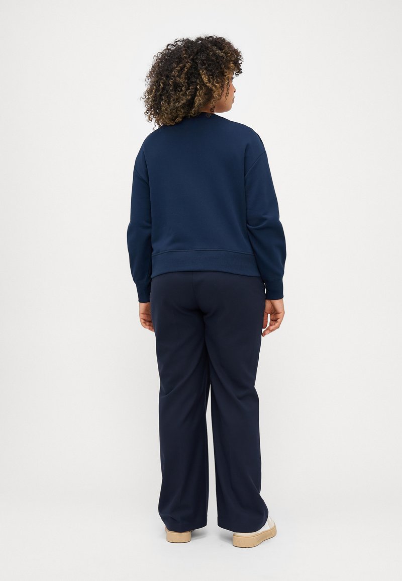 Navyblauwe sweatshirt en bijpassende broek van een zachte stof. De sweatshirt heeft een geribbelde onderkant en manchetten, met een relaxed fit. Platte schoenen maken de look af.
