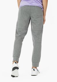 Graue Jogginghosen aus strukturiertem Stoff, mit elastischen Bündchen und Taschen, kombiniert mit weißen Sneakers. Rückansicht gezeigt.