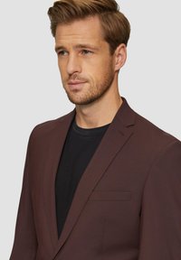 Burgundowy marynarka z wykładanym kołnierzem, pojedynczą kieszenią na piersi i dopasowanym krojem, noszona na czarnym T-shircie. Gładka tekstura materiału.
