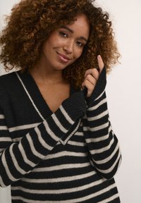 Schwarz-creme gestreifter Pullover mit V-Ausschnitt und geripptem Material. Die Ärmel haben Daumenlöcher, die den Komfort und die Wärme erhöhen.
