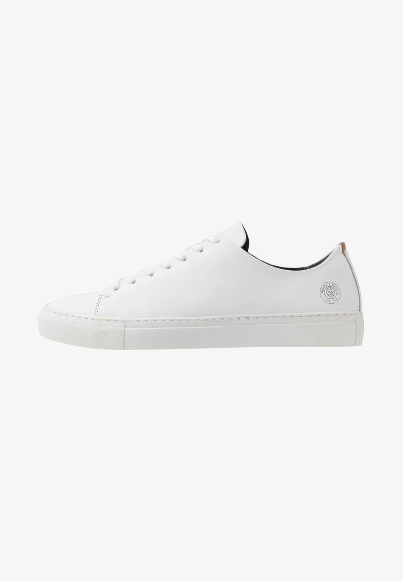 Baskets basses en cuir blanc avec lacets blancs, semelle plate et un petit logo rond sur le côté du talon.