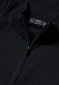 Maglione in lana Merino nera con zip quarti sul davanti e un'etichetta del marchio MNG visibile all'interno del colletto.