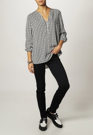 Blusa a righe in bianco e nero con scollatura a V, maniche a tre quarti, abbinata a pantaloni neri aderenti e scarpe bianco e nere.