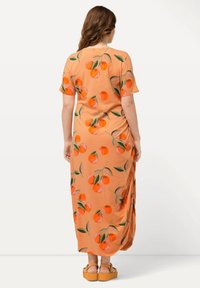 Maxi kjole i peach stof med et levende mønster af orange frugter og grønne blade. Korte ærmer og draperet design. Behagelig pasform.