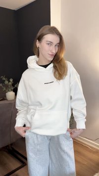 Sweat à capuche blanc avec un logo noir, coupe décontractée, capuche à cordon ajustable et poche avant, associé à un pantalon de survêtement gris.