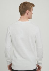 Bela dolga majica s sleeves, ribasto teksturo, okroglo ovratnico in kontrastnimi rokavi. Ponuja čist, minimalističen dizajn.