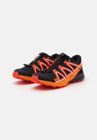 Le scarpe da trail running nere e arancioni presentano un design elegante, una parte superiore in mesh testurizzato e una suola in gomma audace con motivi di aderenza.