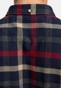 Geruit flanellen overhemd met marineblauwe, rode, witte en grijze kleuren, met een visgraatpatroon en een natuurlijke houten knoop bij de kraag.