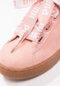 Gros plan d'une basket en daim rose avec une semelle épaisse en gomme et de larges lacets de marque avec le logo Puma en blanc.