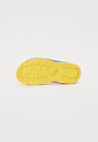 Teva sandal såle, med en rillet gul gummioverflate med trekantede mønstre og en lys blå aksent langs kanten.