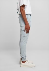 Lyseblå joggebukser med elastiske mansjetter og sidelommer, laget av mykt materiale, kombinert med hvite joggesko.