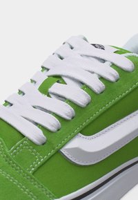 Πράσινο αθλητικό παπούτσι με λευκά κορδόνια και πλευρική ρίγα, κοντινή λήψη στο πάνω μέρος και τις λεπτομέρειες της ραφής.