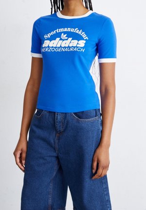 T-shirt bleu à manches courtes avec accents ringer blancs ; comporte l'inscription "Sportmanufaktur adidas HERZOGENAURACH" en lettres grasses sur le devant.