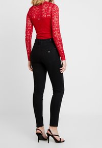 Röd spetsbodysuit med långa ärmar, kombinerad med högmidjade svarta skinny jeans. Svarta klackskor med öppen tå och tunn remdesign.