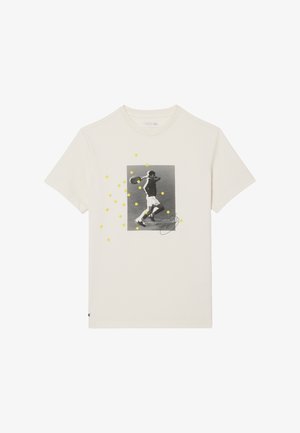 Camiseta color marfil claro con la imagen en blanco y negro de un jugador de tenis en pleno swing, salpicada de puntos amarillos que representan pelotas de tenis.