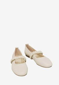 Valkeat ballerinat, jotka on valmistettu sileästä nahasta, varustettu neliönmuotoisella kärjellä, pehmeällä, rypistyneellä remmillä jalkapöydän ylle ja matalalla ruskealla korolla.