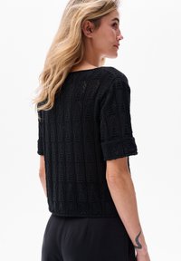 Czarny top z koronką, z geometrycznym wzorem, krótkimi rękawami na rolkę i krótkim krojem, wykonany z teksturowanego, lekkiego materiału.