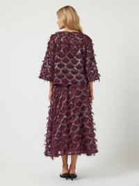 Abito maroon a strati con frange, caratterizzato da un sovrapposto trasparente e maniche larghe. Lunghezza media con una silhouette fluida e tessuto testurizzato.