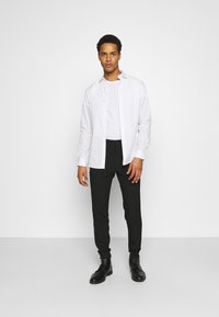 Camisa blanca de botones sobre una camiseta gris, combinada con pantalones negros ajustados y botas negras con cordones. Diseño simple, textura suave.