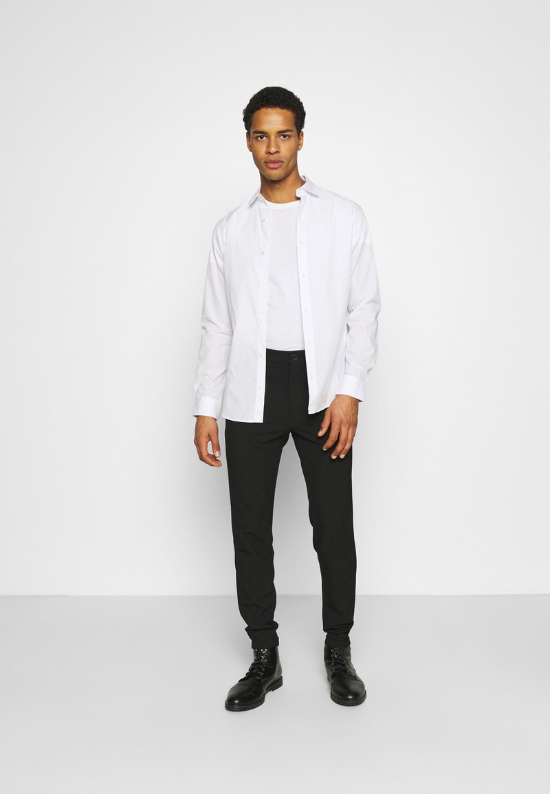 Camisa blanca de botones sobre una camiseta gris, combinada con pantalones negros ajustados y botas negras con cordones. Diseño simple, textura suave.