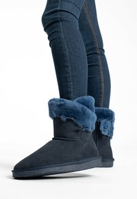 Stivali blu in suede con bordo in pelliccia sintetica, con suola piatta e dettagli cuciti, indossati con leggings in denim scuro.