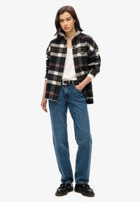Schwarz-weiße karierte Flanellshirt, das über ein weißes T-Shirt getragen wird, kombiniert mit blauen Jeans im Straight-Leg-Schnitt und schwarzen Schuhen.