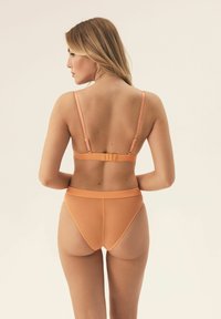 Pomarańczowy zestaw bielizny z miękką, matową teksturą. Biustonosz ma cienkie ramiączka z logo oraz zapięcie na hak, w zestawieniu z majtkami z wysokim stanem.