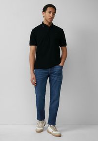 Czarna koszulka polo z krótkim rękawem, proste dżinsy w kroju prostym oraz beżowe sneakersy z białymi akcentami. Prosty design, bez widocznych wzorów.