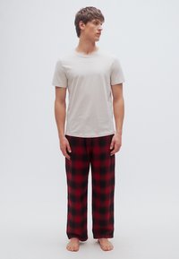 T-shirt gris clair associée à un pantalon de pyjama à carreaux noir et rouge. Les tissus semblent doux avec une coupe décontractée. Le mannequin est pieds nus.