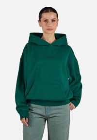 Sweatshirt verde com capuz em corte relaxado, apresentando um bolso canguru e punhos canelados. Feito de um tecido suave e texturizado.