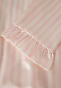 Tissu rayé rose et crème avec une finition satinée. Présente un bord froncé le long de la manche et une texture lisse.