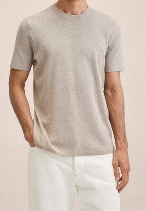Beige short-sleeve t-shirt in a soft, textured fabric with a round neckline, paired with white trousers. Simple, clean design.