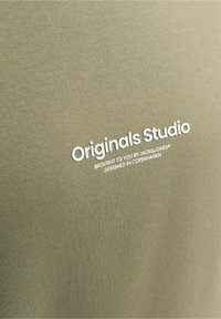 Tissu vert olive avec texte blanc « Originals Studio » et texte plus petit « Offert par Jack&Jones, conçu à Copenhague »