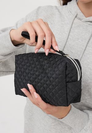 Borsa cosmetica nera trapuntata con chiusura a zip e manico, caratterizzata da una superficie testurizzata e forma rettangolare. Rifiniture con cuciture chiare.