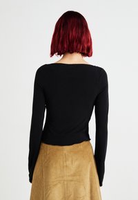 Musthave musta pika varrukaga topp avatud kaelusega, millele on kombineeritud tekstuuriga beezist puuvillast mini-seelik, millel on sile viimistlus.