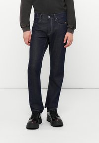Mørkeblå denim jeans med rett benkutt, fem-lomme-design og kontrasterende søm. Kombinert med svarte snøresko.