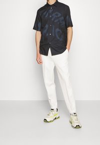 Košile s krátkým rukávem, tmavě modrá, s velkým průhledným grafickým potiskem. V kombinaci s bílými, zúženými kalhotami a lehkými teniskami.