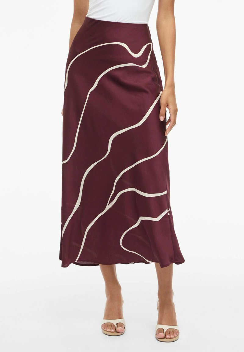 Bordeaux satin maxi nederdel med creme farvet bølget mønster, glat overflade, høj talje og en flagrende kant, parret med beige strop-sandaler.