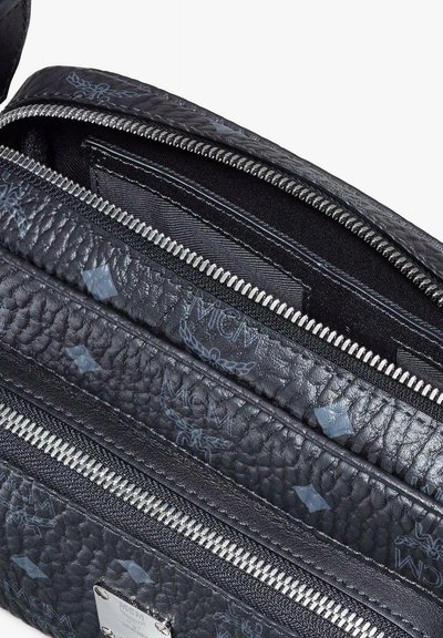 Borsa in pelle nera testurizzata con cerniere argentate e logo e simboli MCM blu chiaro, parzialmente aperta per mostrare la fodera in tessuto interna.