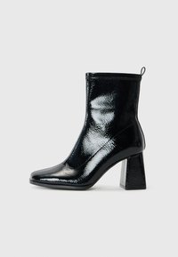 Bottine en patin noir avec un bout carré et un talon géométrique épais. Présente une texture lisse et brillante ainsi qu'une languette à l'arrière pour un enfilage facile.