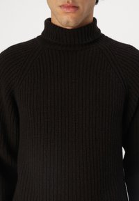 Donkerbruin gebreid coltrui met ribbelstructuur en raglanmouwen, voorzien van een hoge kraag en een slim-fit ontwerp.