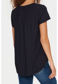 Top corto nero con scollo arricciato e una leggera texture, caratterizzato da una vestibilità morbida e un orlo curvo, abbinato a jeans blu.