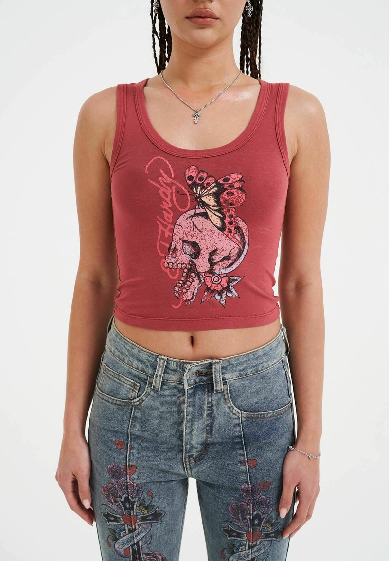Top rojo sin mangas con un diseño gráfico que presenta un cráneo, una mariposa y acentos florales. Combinado con unos jeans de mezclilla desgastados de tiro alto.