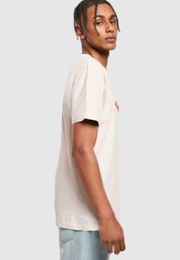 Light beige cotton t-shirt with short sleeves and simple round neckline. Features red lettering on the front and a relaxed fit.