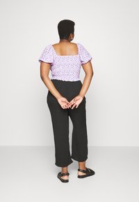 Top de estampa floral roxa com mangas bufantes e costas franzidas, combinado com calças pretas fluídas e sandálias pretas. Modelo mostrado de costas.