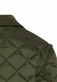 Donkergroene gewatteerde jas met diamond stitching op de schouder en een geribbeld kraagdetail op een witte achtergrond.