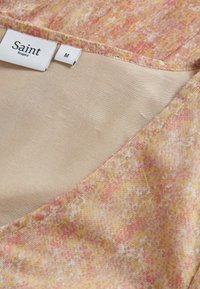 Flerfärgad topp i pastellnyanser av rosa och gult, gjord av lättviktsmaterial med en slät halsringning och en etikett med texten "Saint Tropez", storlek M.