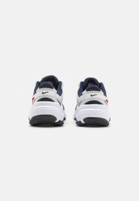 Ett par vita, marina och röda Nike-sneakers visade från baksidan på en vit bakgrund, som framhäver tjocka sulor och logodetaljer.