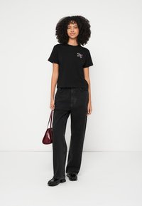 Svart bomulls-T-skjorte med korte ermer og tettsittende design; har et fargerikt brodert motiv på brystet. Kombinert med høytlivs svarte jeans.