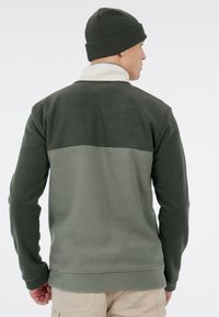 Fleece pullover in donkergroen en lichtgroen, met een hoge kraag en geribde zoom. Vergezeld van een bijpassende groene beanie.